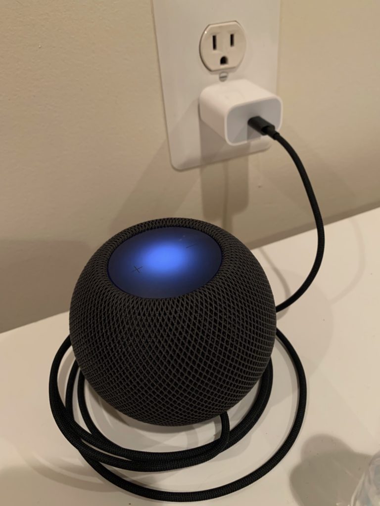 An Apple HomePod mini installed on a bookshelf.